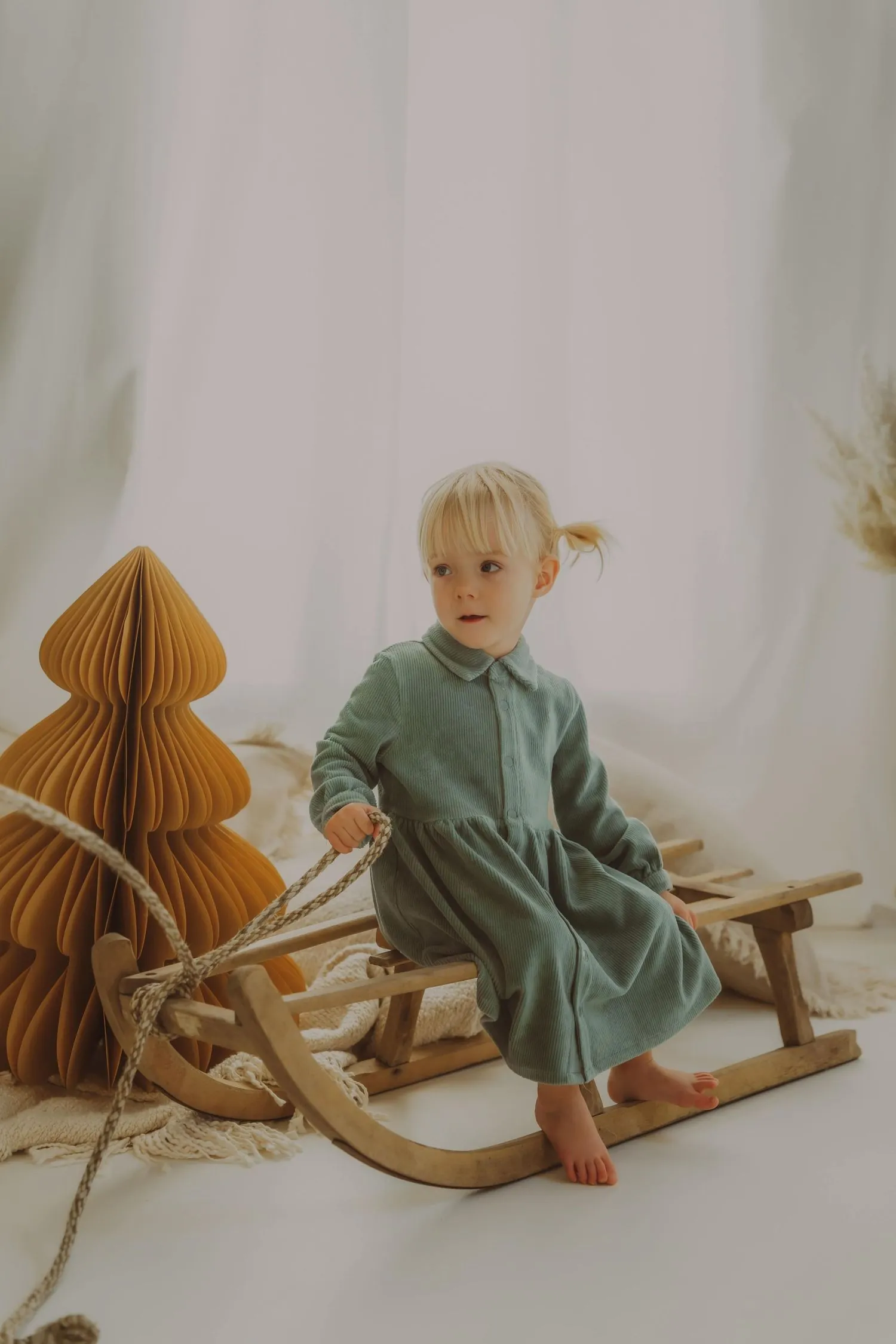 Enfant en robe vert sauge sur un cheval à bascule en bois