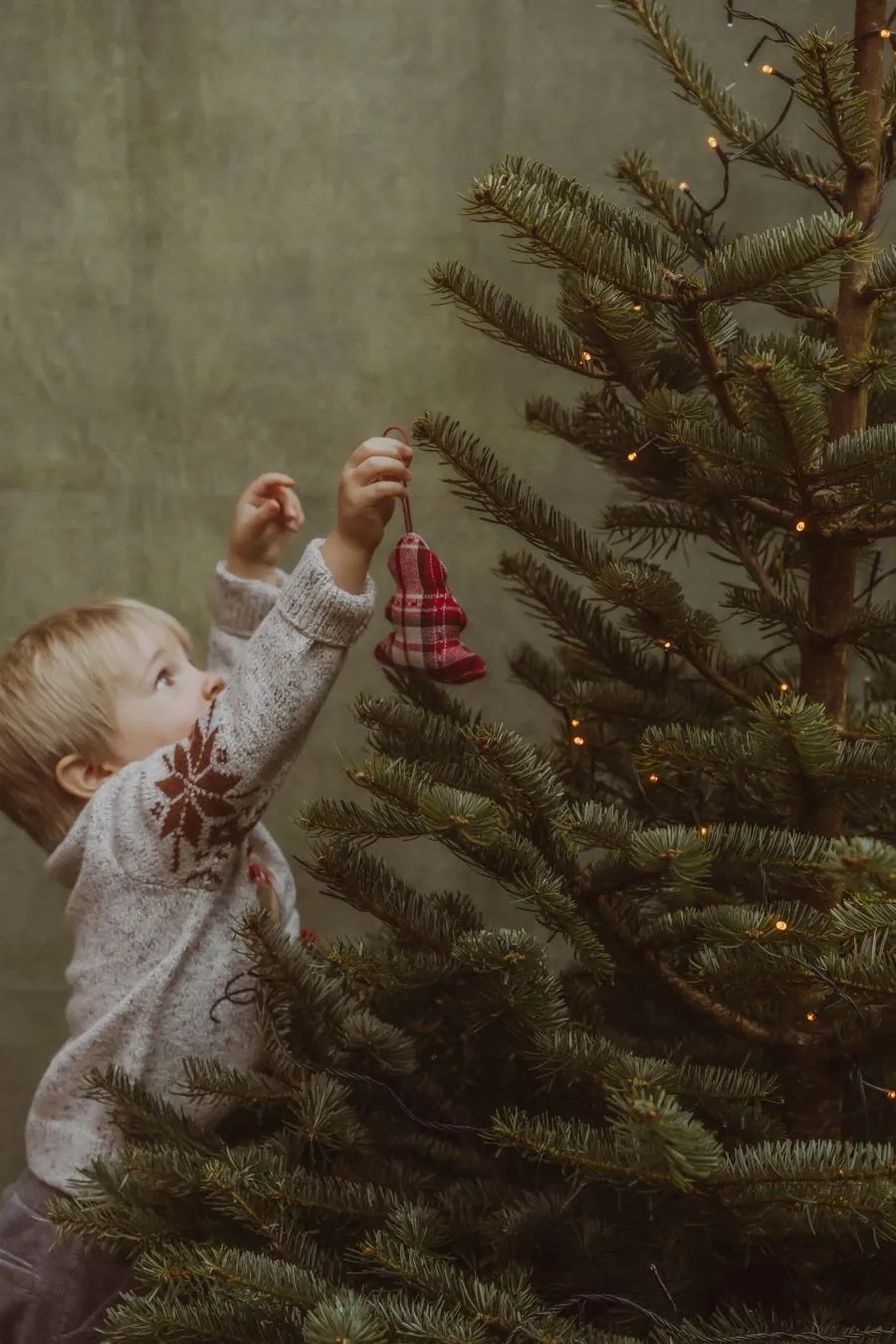 Enfant en pull blanc accroche des boules dans le sapin