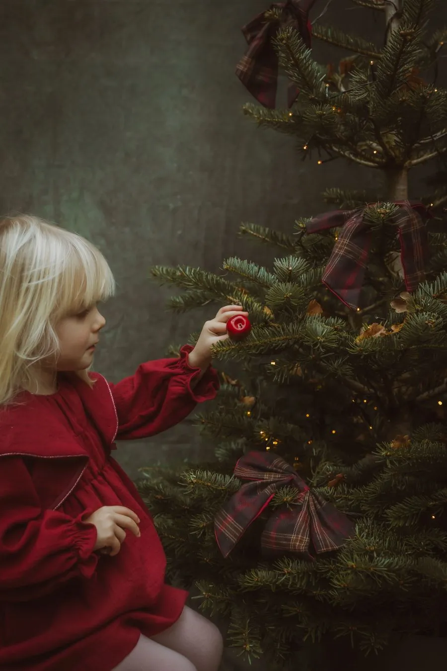 Enfant en pull rouge accroche des boules dans un décor chaleureux