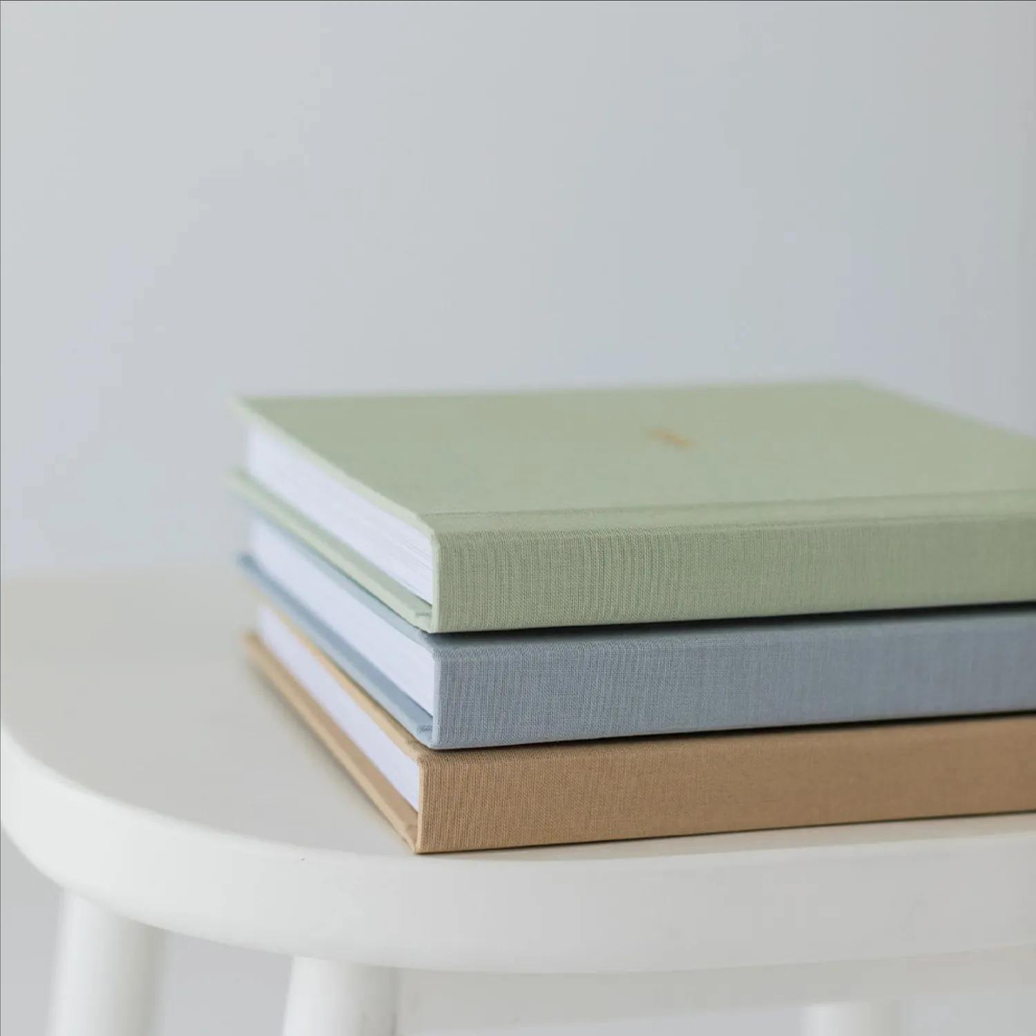 Three linen albums stacked, in green, blue and beige