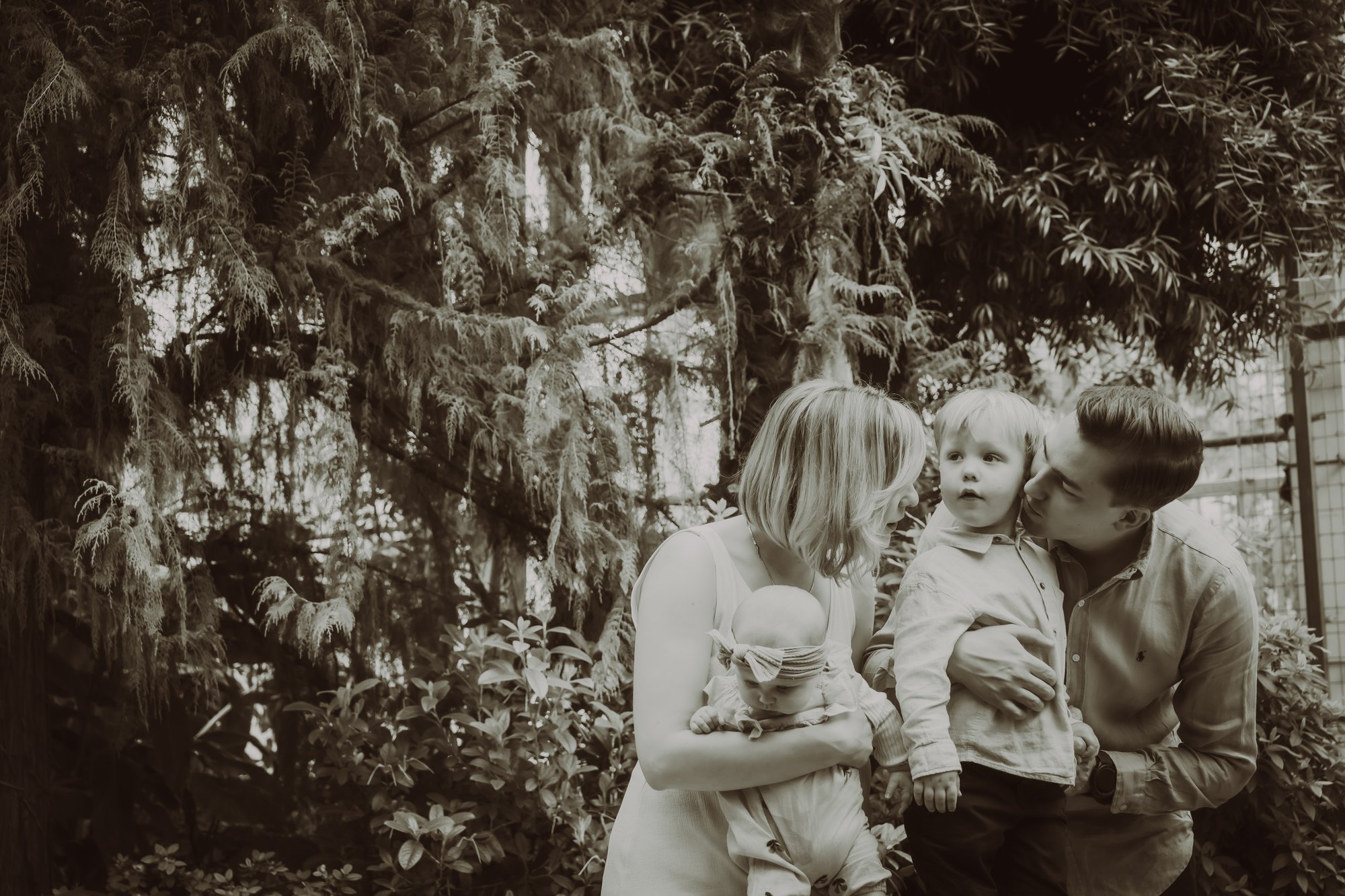 Candid gezinsportret in het groen — moeder, vader en kinderen tussen het gebladerte